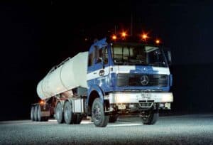 Blue Mercedes-Benz tank truck with illuminated warning lights at night.