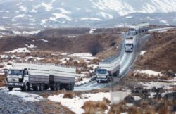 A line of trucks traveling through a snow-covered mountain landscape, showcasing rugged terrain and challenging driving conditions. Truck convoy on snowy mountain road in New Zealand.