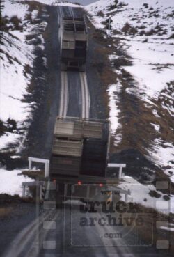 A large truck with a trailer sliding down a snowy mountain slope, illustrating a severe accident scenario. Heavy truck accident on icy mountain slope with trailer derailment.