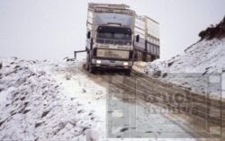 A large truck driving through a snowy, mountainous terrain in New Zealand, emphasizing durability and off-road performance. Heavy-duty truck driving on snow-covered mountain road, showcasing rugged transport capabilities.