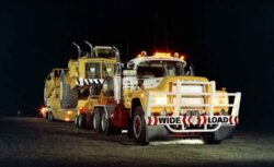 A large yellow tow truck with flashing lights on a dark night, ready to assist with vehicle recovery. Heavy-duty tow truck with bright lights at night for vehicle recovery.