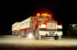 A powerful Mack truck with flashing lights parked at night, highlighting heavy-duty transport capabilities. Mack heavy-duty truck with flashing lights parked on a dark night, suitable for transport and logist.