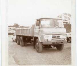 An old black-and-white photograph of a vintage truck parked outdoors, with other vehicles and signage in the background. Classic vintage truck for sale at TruckArchive, highlighting historical commercial vehicle models.
