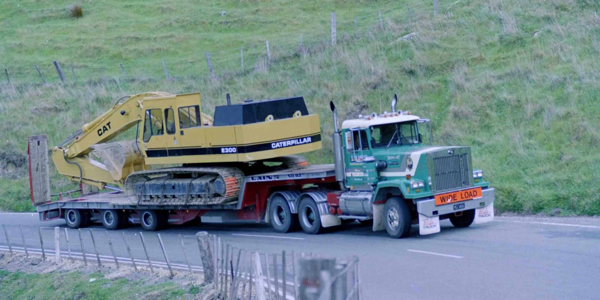 Heavy machinery transport featuring a Caterpillar excavator on a flatbed truck.